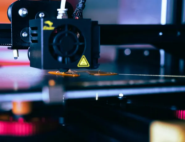 A 3D printer with a hazard sign and melting plastic on an extruder table.