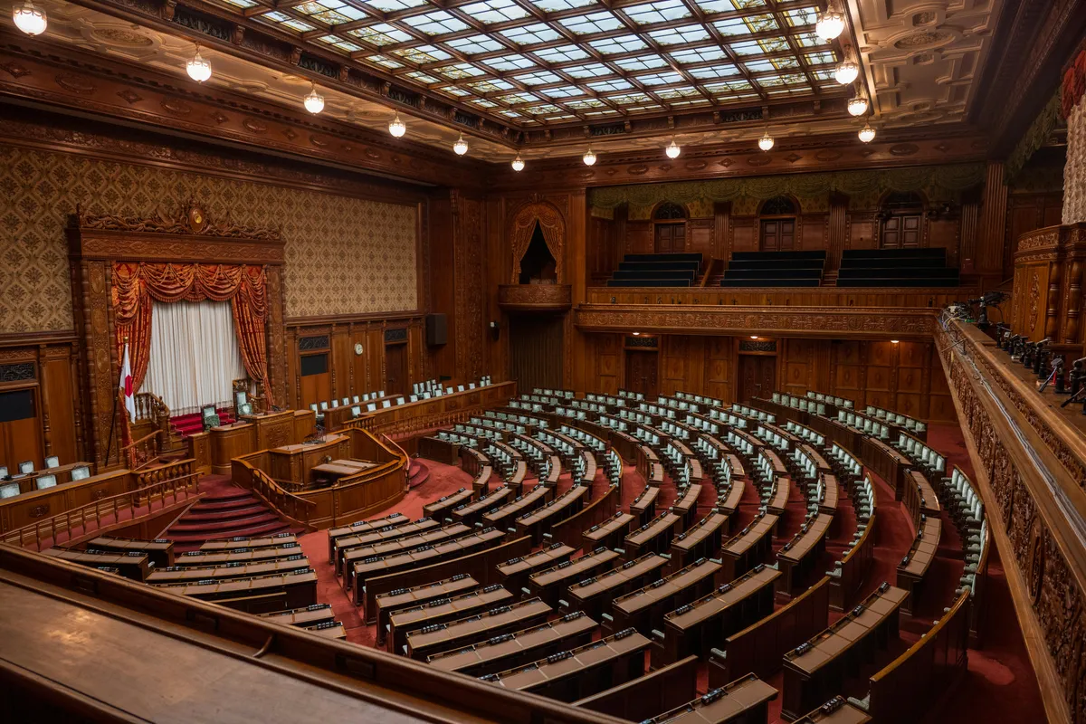 The empty wood-paneled chamber of Japan's National Diet, semicircular desks beneath a glass skylight.