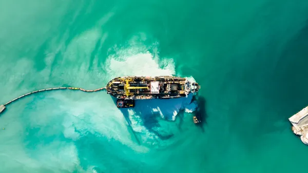 Aerial view of a cable-laying ship trailing its cable across open water to shore, the global network stitched line by line.