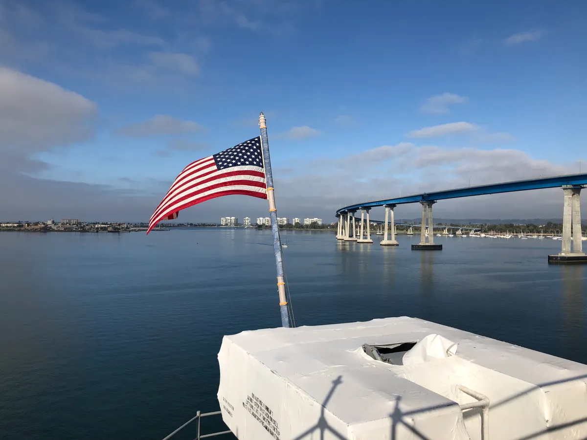 American flag flying from the aft of USS Boxer, in port San Diego, looking across at the Coronado Bridge.